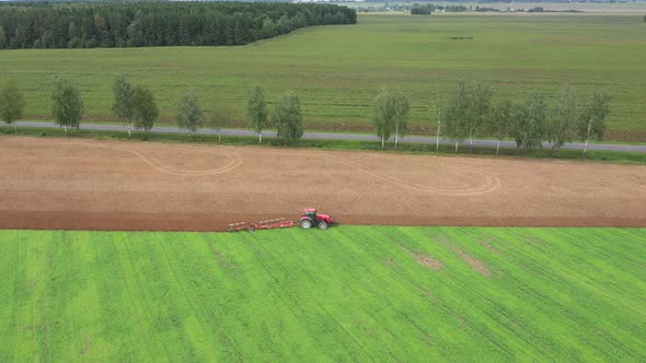 Tractor Ploughs A Green Agricultural Field For Planting Crop Aerial View