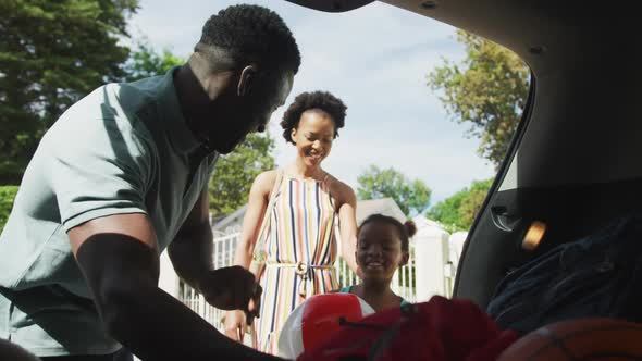 Happy african american family packing car with beach balls on holiday