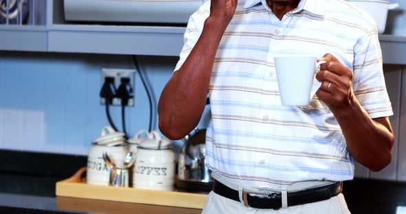 Senior man talking on mobile phone while having coffee in kitchen