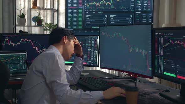 Disappointed Of Asian Male Stock Market Broker Analyzing Graphs On Multiple Computer Screens