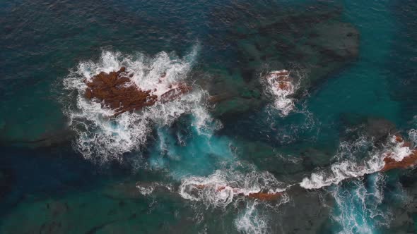 Aerial top down submerged rocks waves breaking on translucent turquoise water