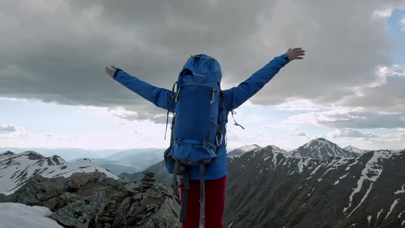 Young Happy Woman with Backpack Standing on a Rock with Raised Hands and Looking To a Valley