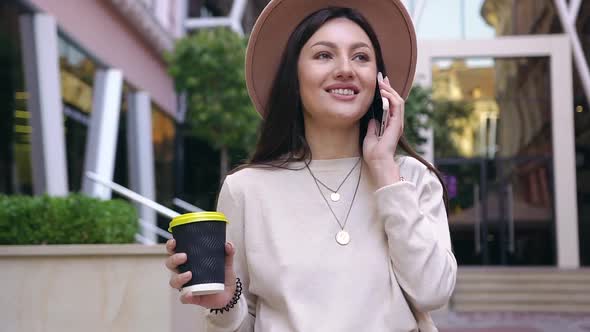 Young Lady in Lovely Hat with Her Fresh Coffee in Hand Talking on Phone