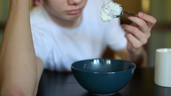 plate with rice porridge. Teen lazily picking porridge with a spoon