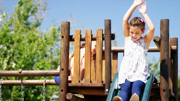 Happy schoolgirl playing on slide in playground