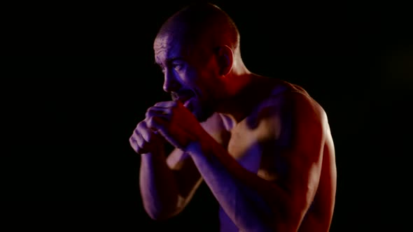 a Muscular Man with a Naked Torso Strikes with His Hands on a Dark Background