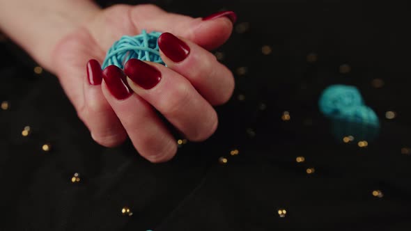 Mature Woman's Hand with Red Polish Nails Holds Braided Ball on Black Background
