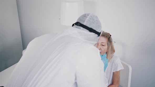 Nurse in Protective Suit Performing Nasal Swab Coronavirus Test on an Old Woman with Face Mask