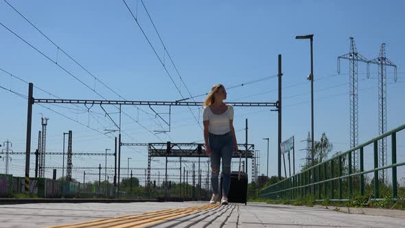 A Young Beautiful Woman with a Suitcase Walks Along a Deserted Train Station Platform