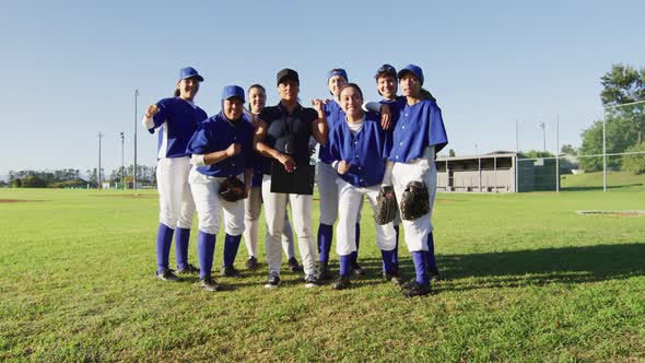 Portrait of diverse team of female baseball players and coach on pitch, raising fists and cheering