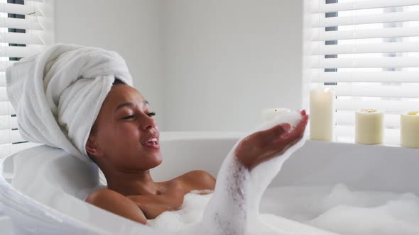 African american woman blowing soap bubbles in the bath tub in the bathroom at home