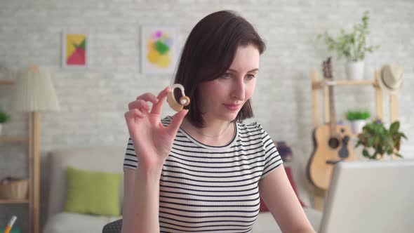 Young Woman Looking for Information on the Internet in a Laptop and Holding a Hearing Aid Close Up