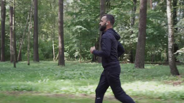 Man Running Through Summer Forest Camera Following Runner in Wireless Headphones Healthy Lifestyle