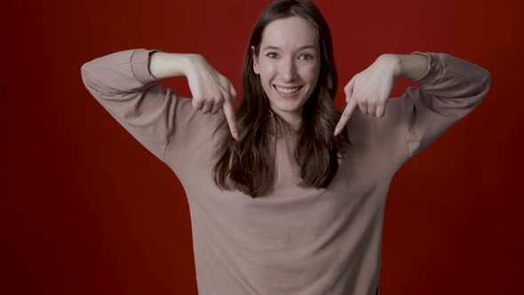 A Positive Young Woman Points Her Fingers Down Indicating a Spot for your Advertisement