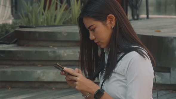 Asian Attractive Young Woman with Glasses Uses Phone on the Street