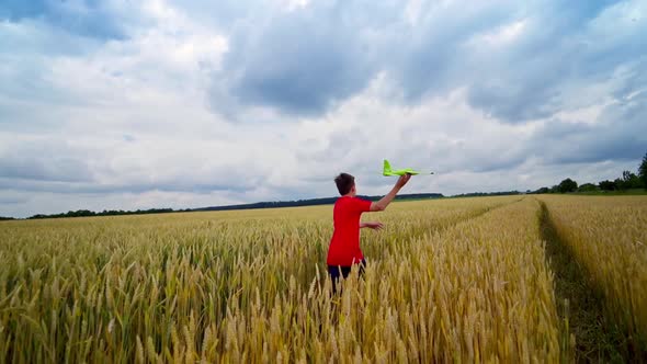 Boy launching toy plane in the field. Teenager runs with plane on yellow field under blue sky. Happy