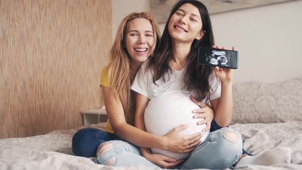 Beautiful Pregnant Woman Holding and Looking Ultrasound Photo Newborn Baby Together with Girlfriend