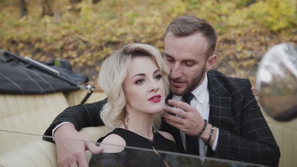 Handsome Gentleman Whispers in Lady's Ear with Smile in Retro Cabriolet