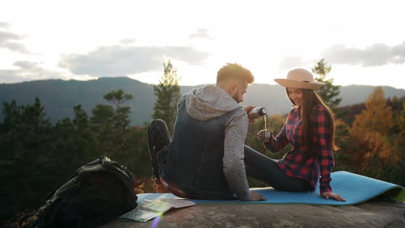 A Young Woman and a Man are Sitting on a Large Rock