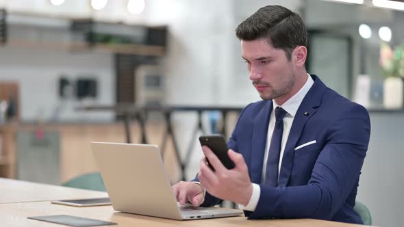 Businessman Using Smartphone and Laptop in Office 