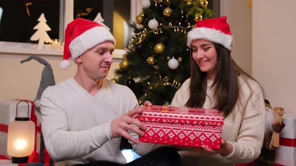 Beautiful Young Couple Opening a Gift Box Enjoy the Winter Holidays Near the Christmas Tree