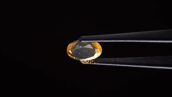 Natural Yellow Fire Opal Gemstone in the Tweezer on the Background