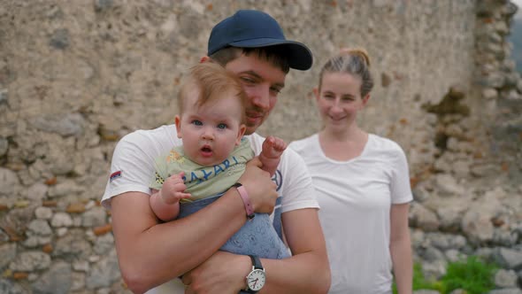 Father Holds Baby Girl Near Mother Standing Against Ruins