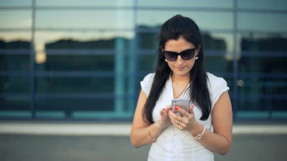 Businesswomen Working with a Mobile Phone in the Street with Office Buildings in the Background