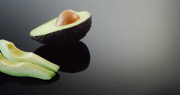 A ripe avocado with the pit and two slices ready isolated on a black mirror background.