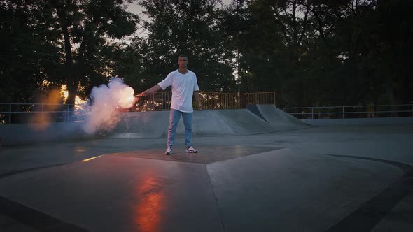 Young Man in Casual Clothes is Holding Glowing Red Signal Flare and Going to Perform Breakdance on