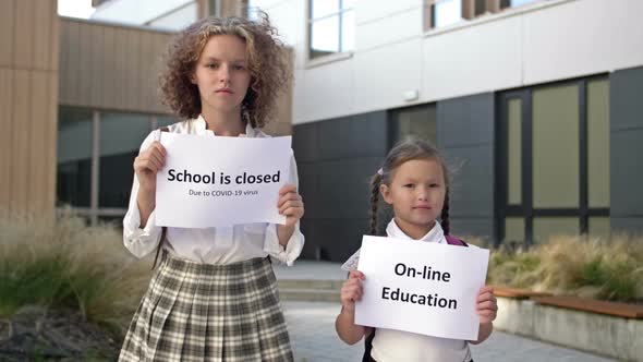 Two Schoolgirls with Placards are Standing in Front of the School Building