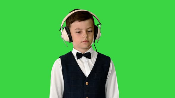 Boy in a Bow Tie Listening To Music Keeping Hands on the Headphones on a Green Screen Chroma Key