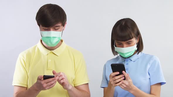 Man and Woman in Sterile Masks Looking at Phones and Terrifiedly Looking at Each Other