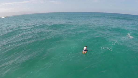 Aerial view of man sitting on board waiting for waves stand-up paddleboard surfing in Hawaii.