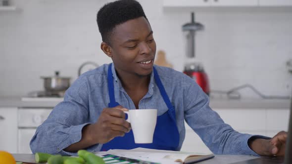 Happy Young Male Freelancer Typing on Laptop Keyboard Holding Morning Coffee Cup