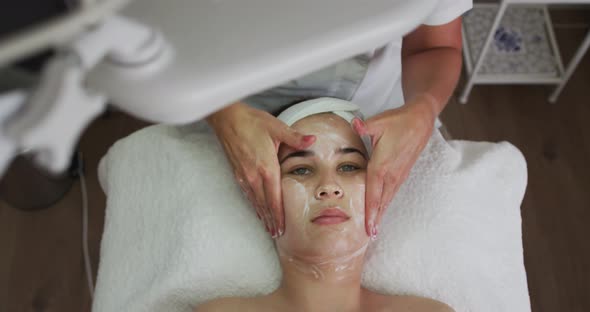 Caucasian woman lying back while beautician gives her a facial