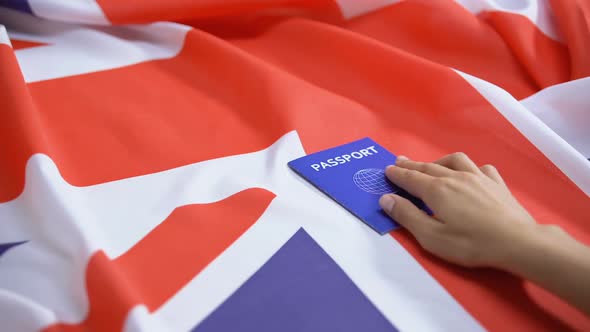 Female Hand Putting International Blue Passport on British Flag, Visa Applicant
