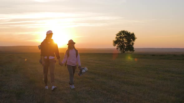 Mother and Daughter with Backpacks Running Through the Meadow at Sunset. Family Tourism Concept.