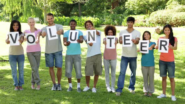Group of Casual Young Friends Smiling at Camera Holding Letters Spelling Volunteer