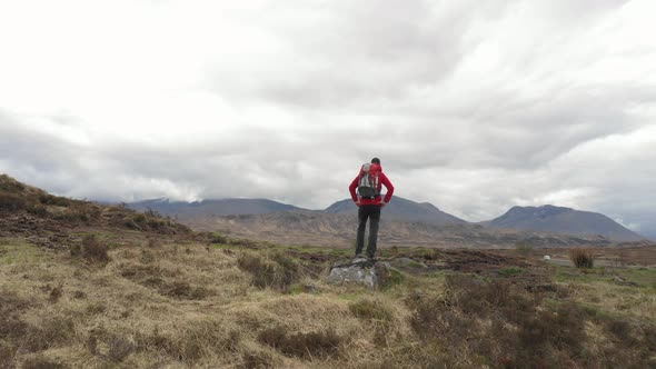 Successful man with backpack exploring Highlands in Scotland and raising hand