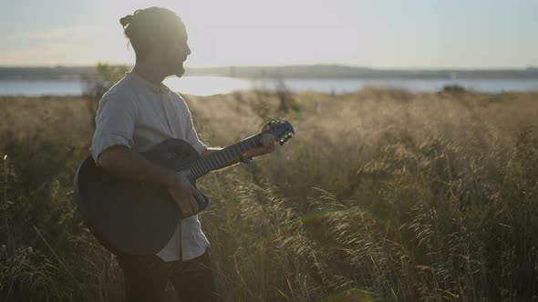 Sihouette of Spanish Male Guitarist Playing Chords and Singing Song in the Middle of Grassy Meadow