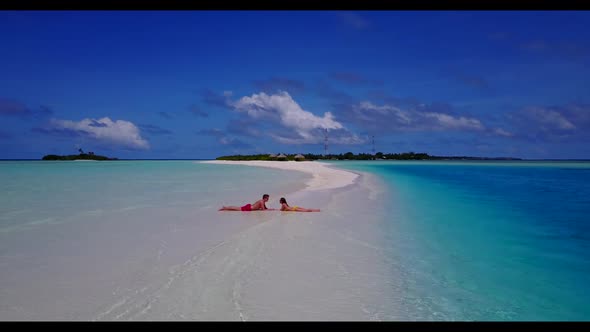 Two lovers sunbathe on exotic tourist beach adventure by aqua blue water with white sandy background