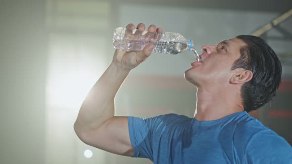 Caucasian young male athlete or sportsman standing in fitness or gym  drinking a bottle of water.