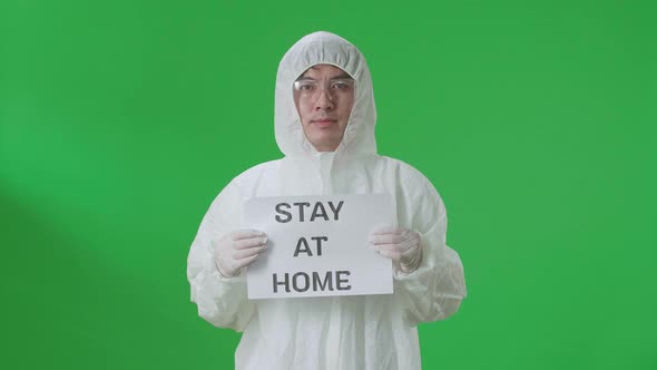 Asian Man Wearing Protective Uniform Ppe And Holding Stay At Home Sign In The Green Screen Studio