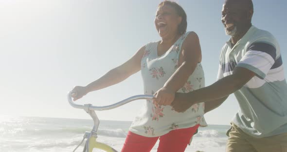 Smiling senior african american couple riding bicycles on sunny beach