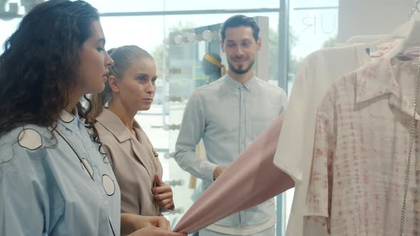 Friendly Salesman Talking to Female Customers Choosing Clothes and Using Tablet in Store