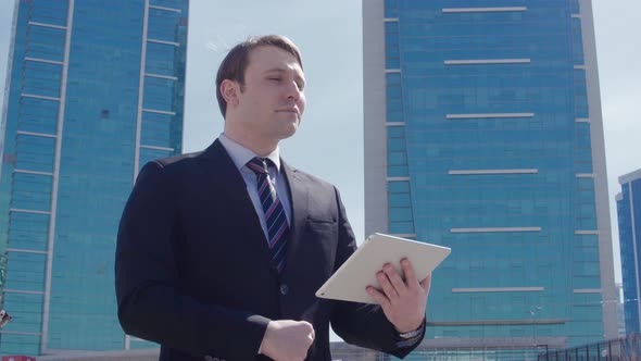 Businessman working with tablet in front of business buildings.