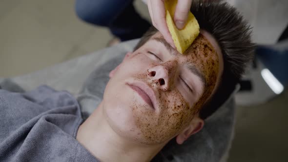 Beautician's Hands Clean the Man's Face with Sponge From a Coffee Scrub