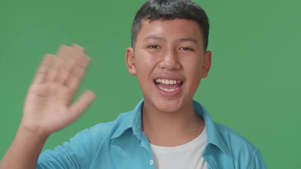 The happy young Asian man waving hand while standing on green screen in the studio