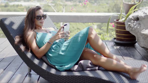 Attractive Woman with Smartphone Resting on Chaise Lounge